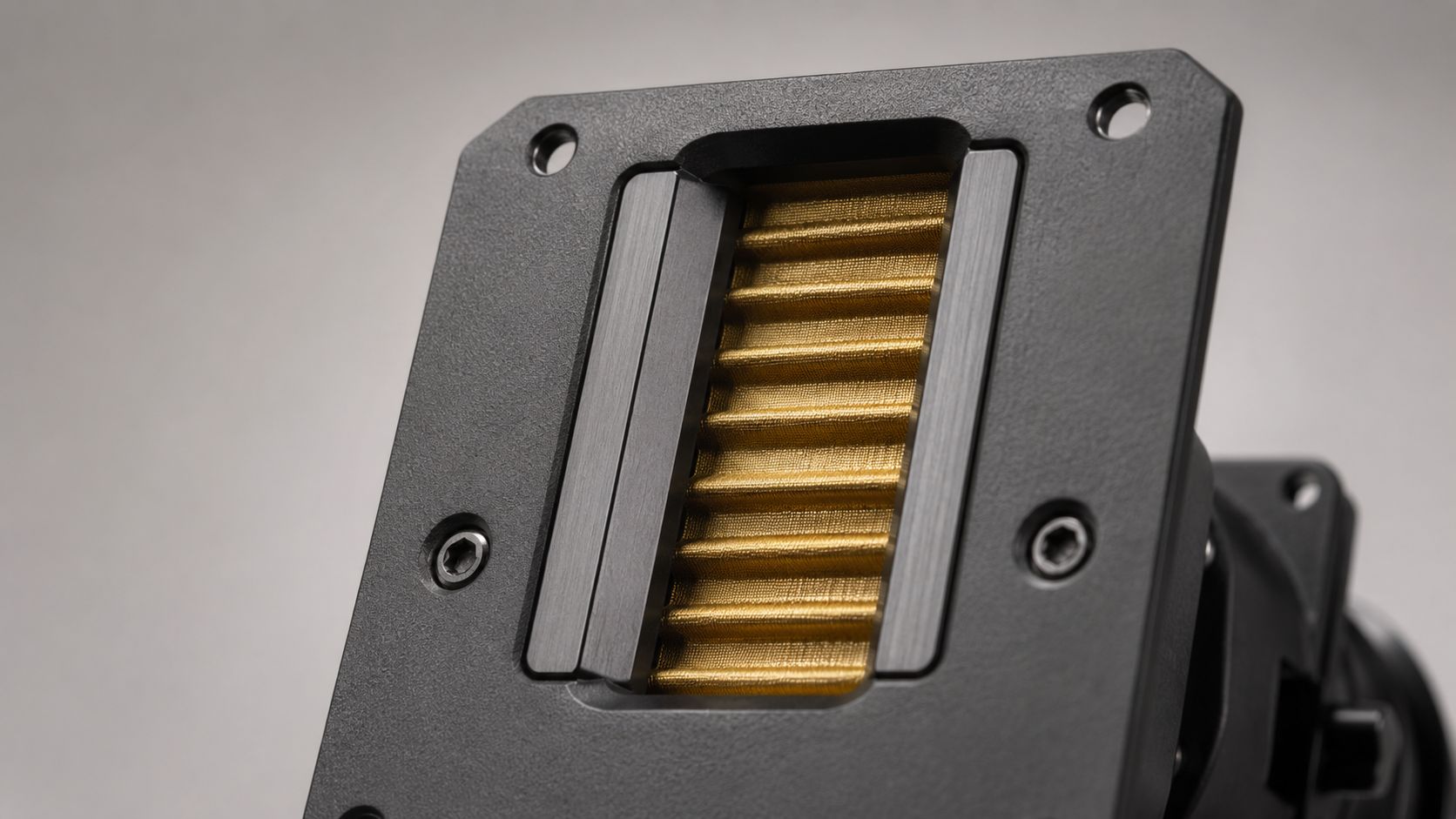 A close-up view of an air motion transformer tweeter with a pleated gold diaphragm and black metal housing.