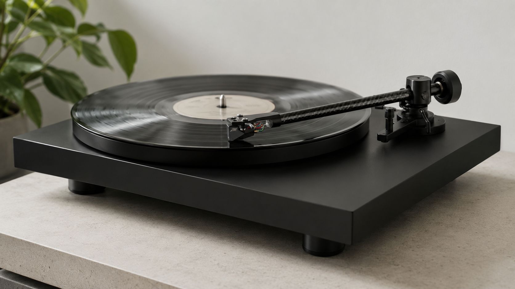 A modern black record player with a carbon fiber tonearm playing a vinyl record on a table.
