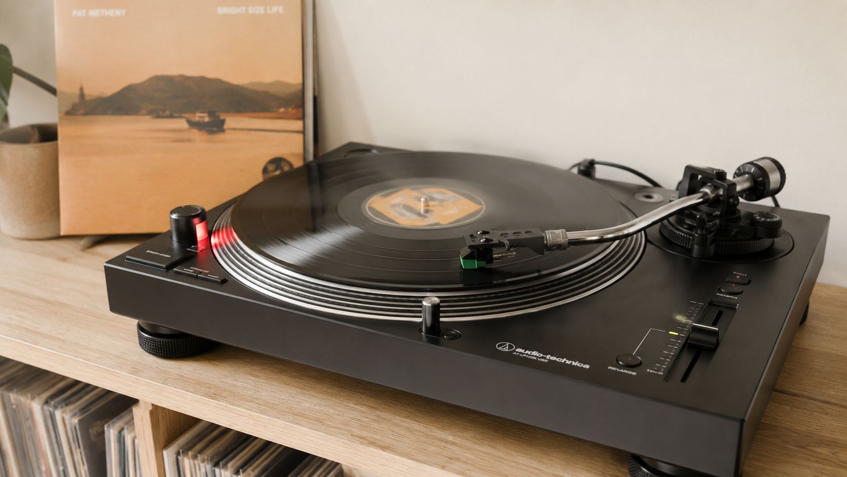 An Audio-Technica turntable playing a Pat Metheny Bright Size Life vinyl record on a wooden shelf.