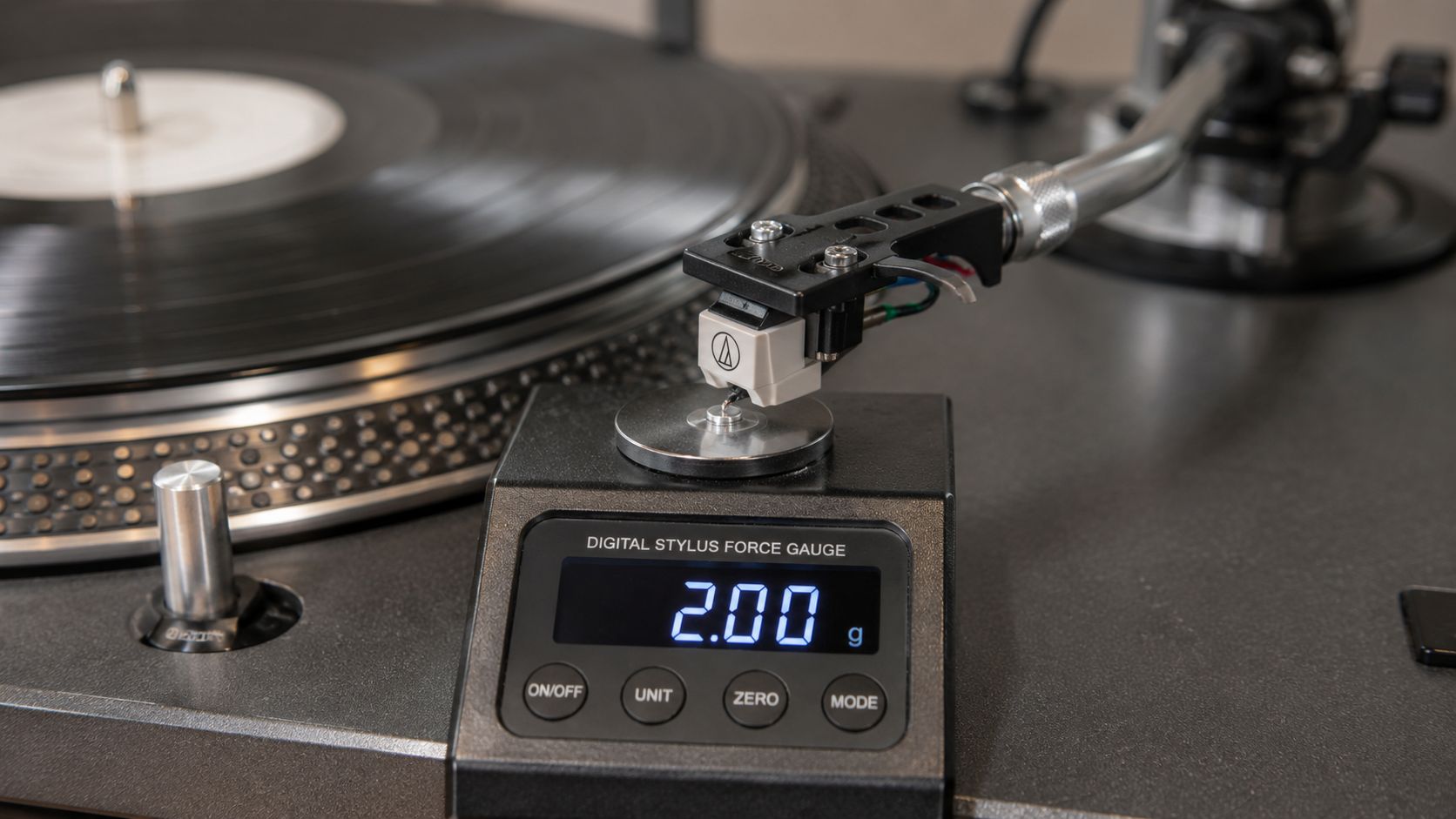 A close-up of a digital stylus force gauge measuring the tracking weight of a turntable tonearm and cartridge.