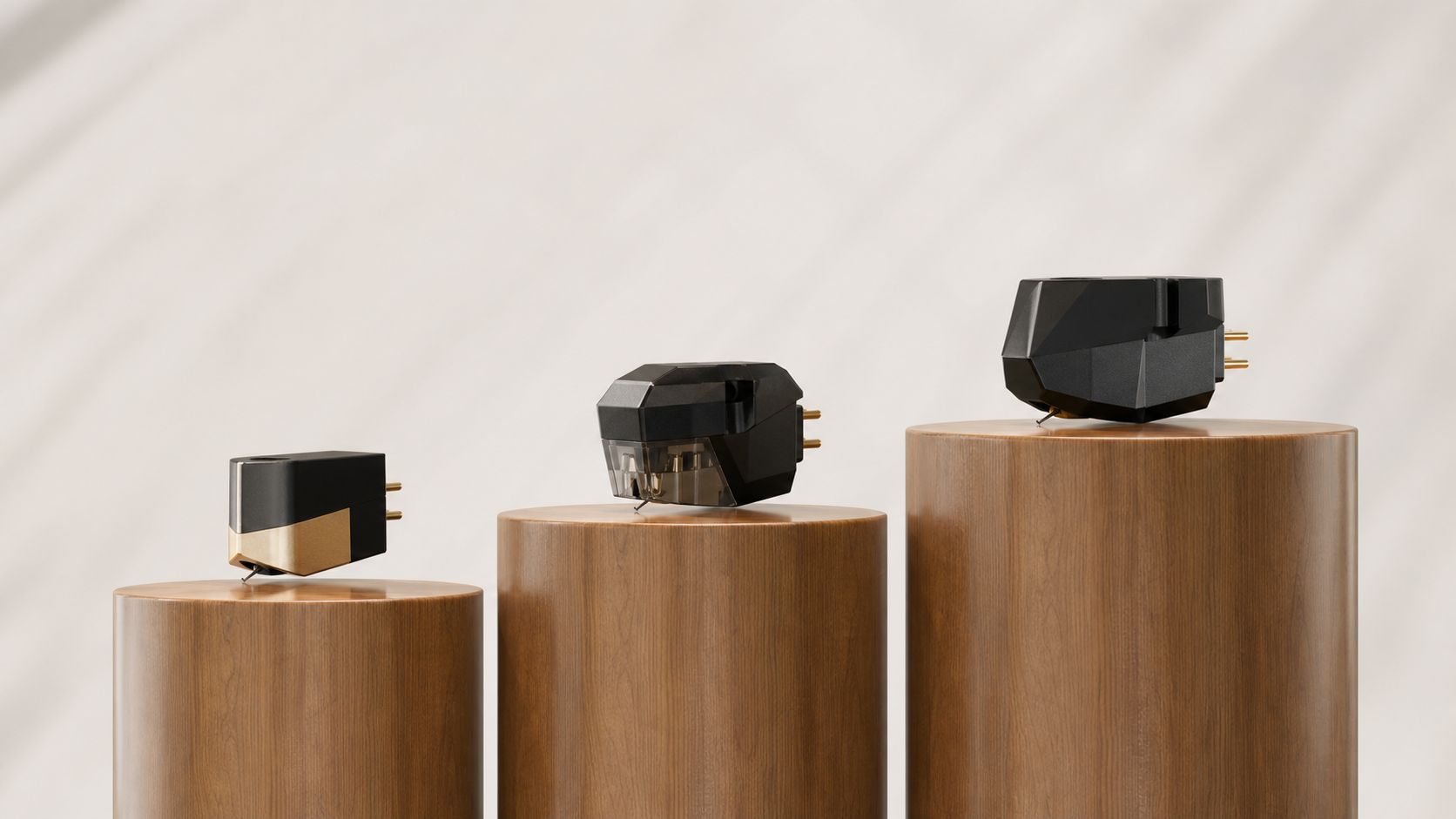 Three high-end turntable cartridges displayed on individual wooden cylinders against a soft, light-colored background.