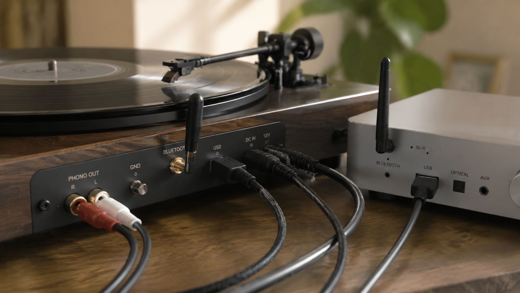 A wooden turntable connected via cables to a silver audio amplifier on a wooden surface.