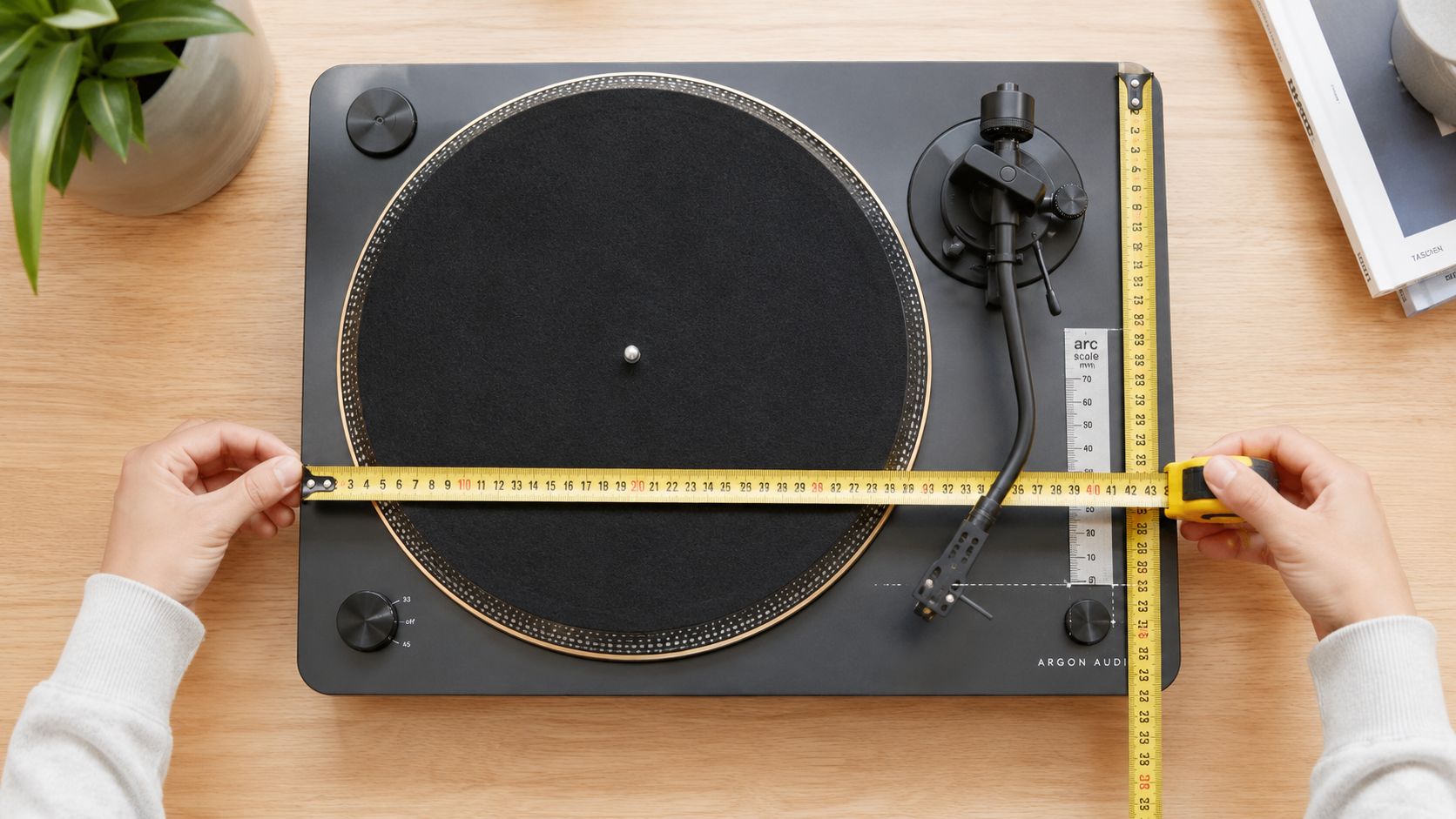A top-down view of a black record player being measured with a yellow tape measure on a wooden surface.