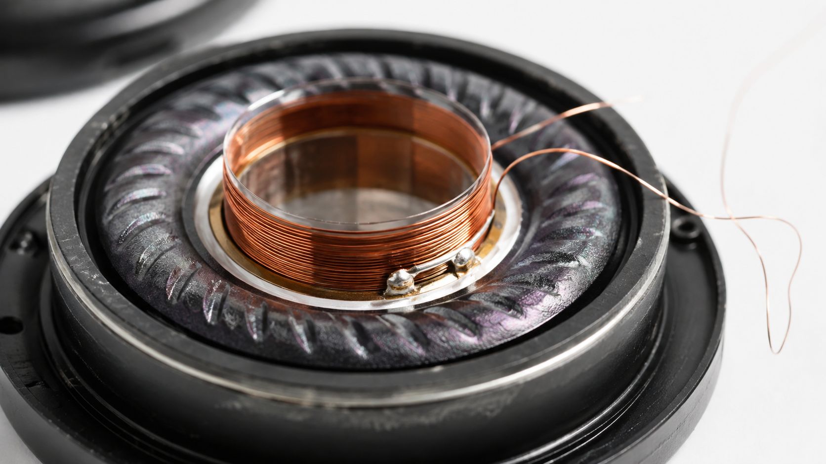 A close-up view of the internal copper voice coil assembly inside a dismantled headphone speaker driver unit.