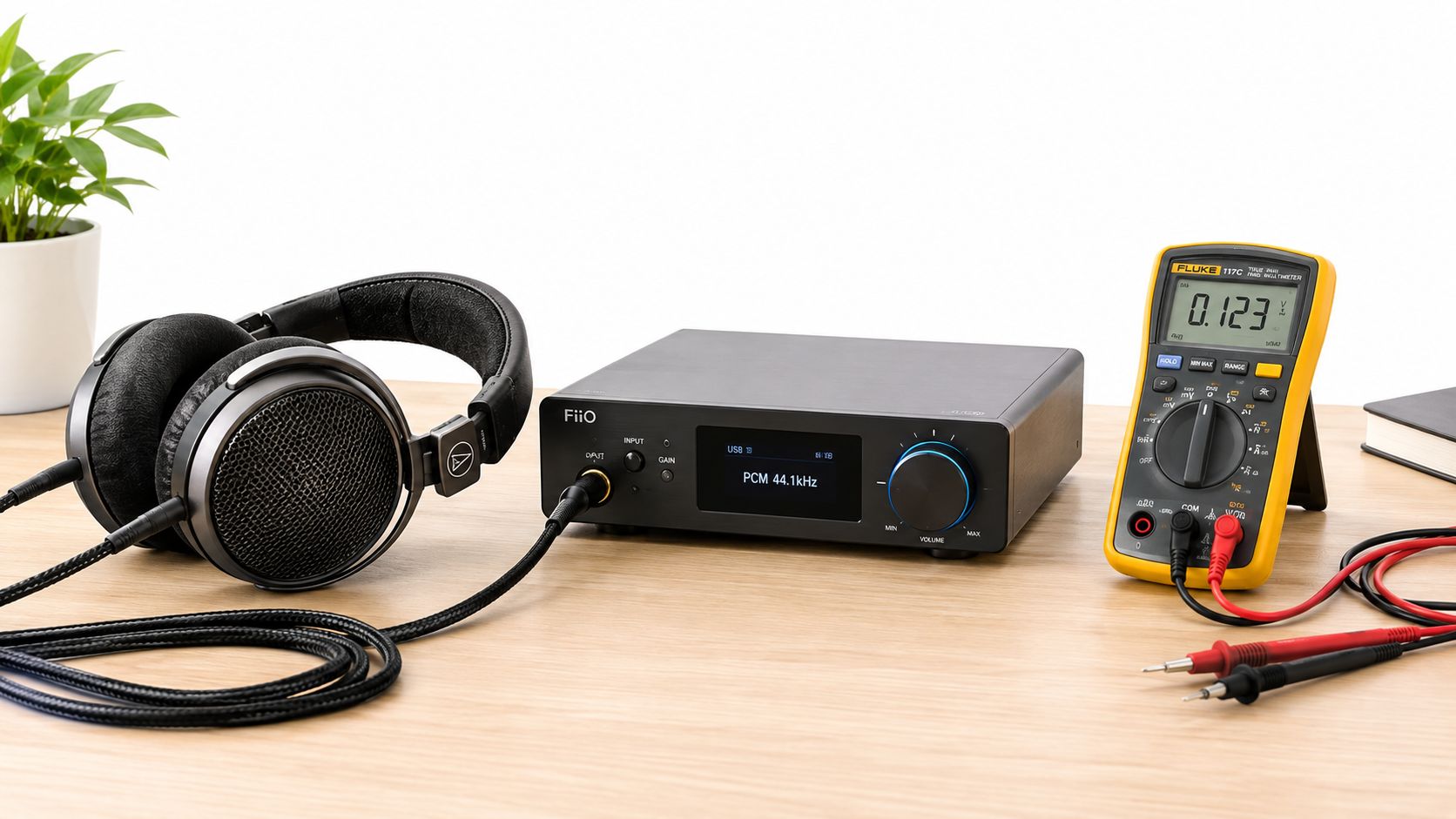 A FiiO headphone amplifier connected to Audio-Technica headphones, with a digital multimeter on a wooden desk.