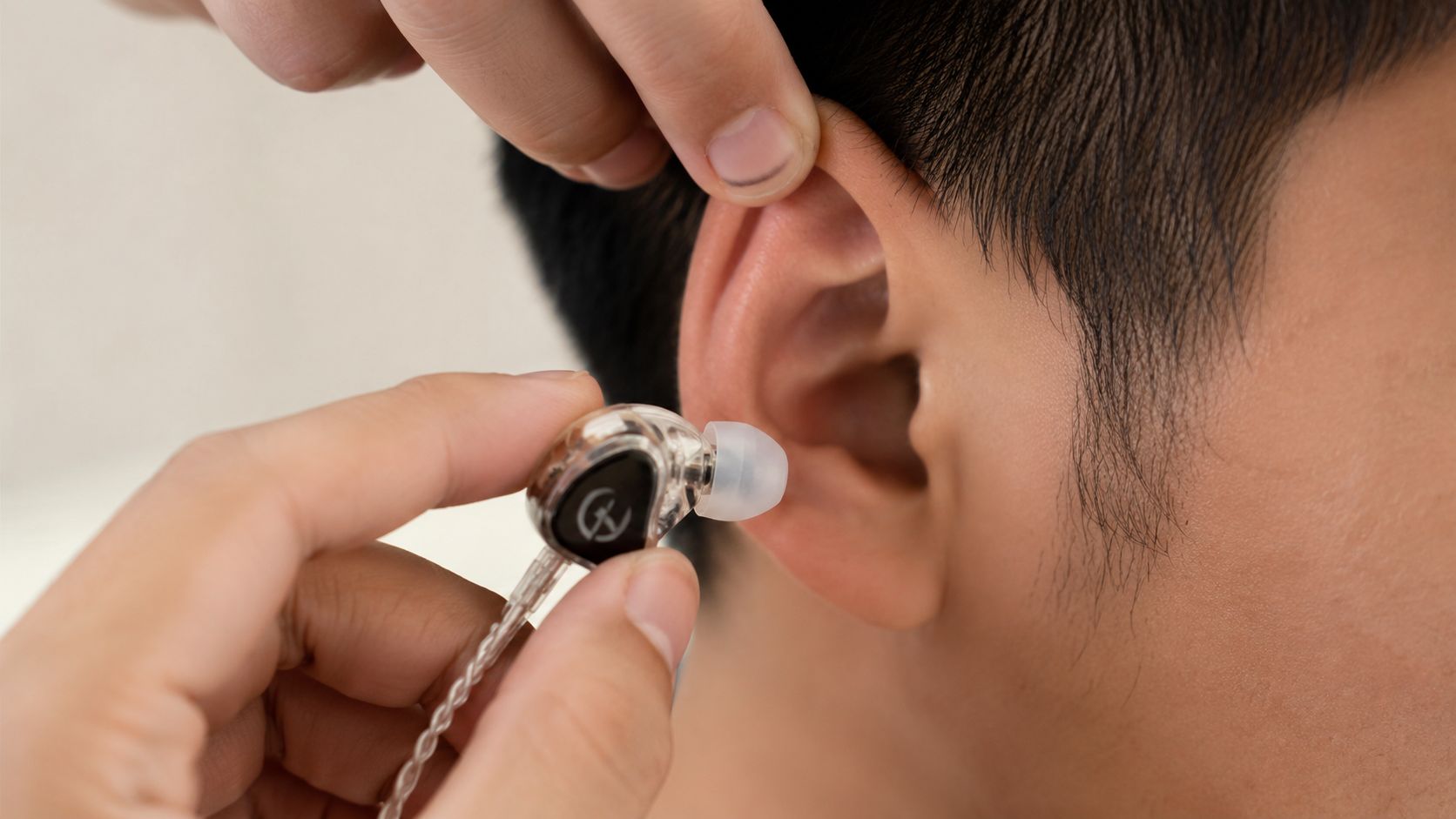 A person carefully inserting a high-quality transparent in-ear monitor into their ear for optimal sound performance.