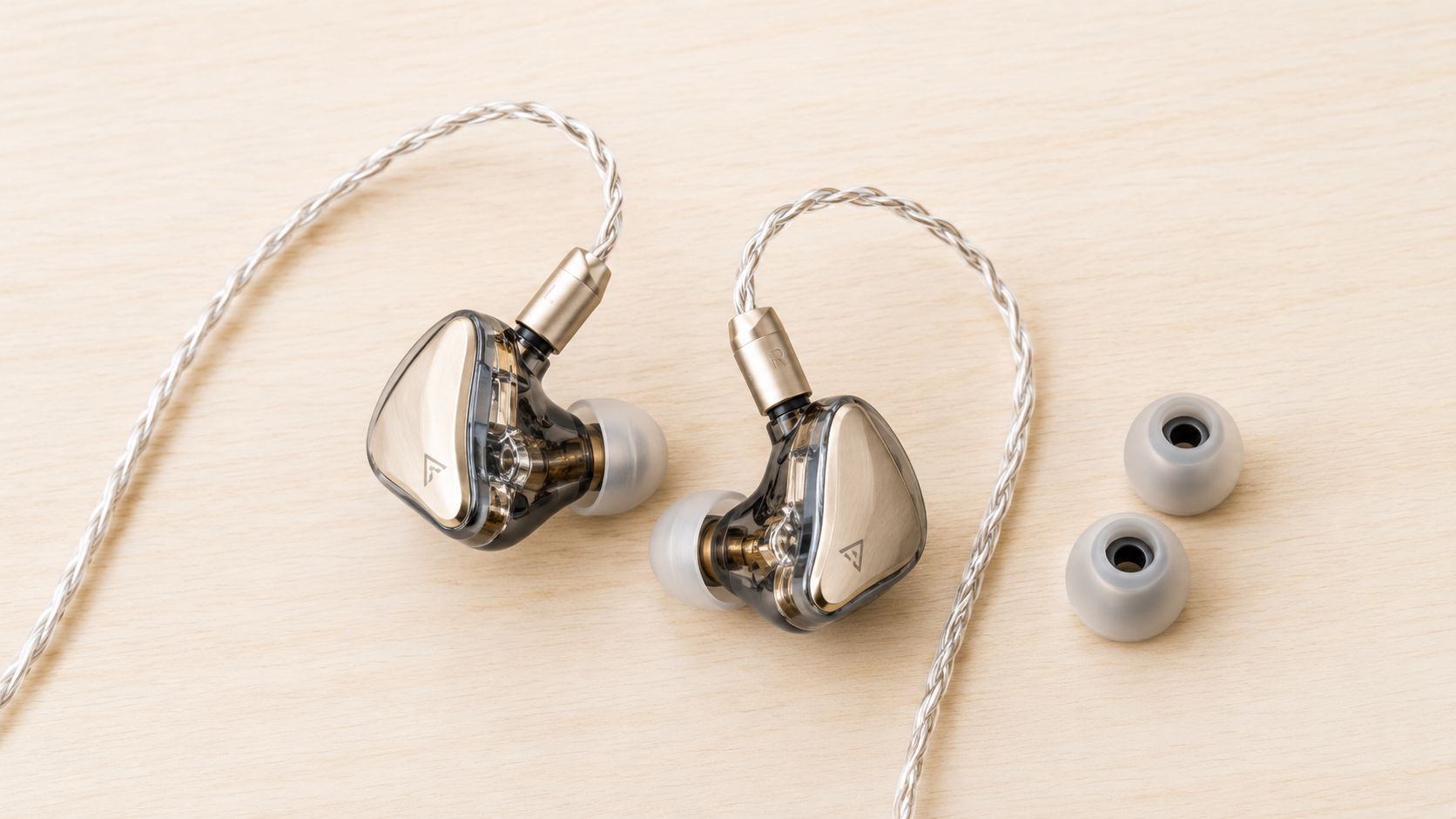 A pair of premium wired in-ear monitors with gold faceplates and a braided cable on a wooden surface.
