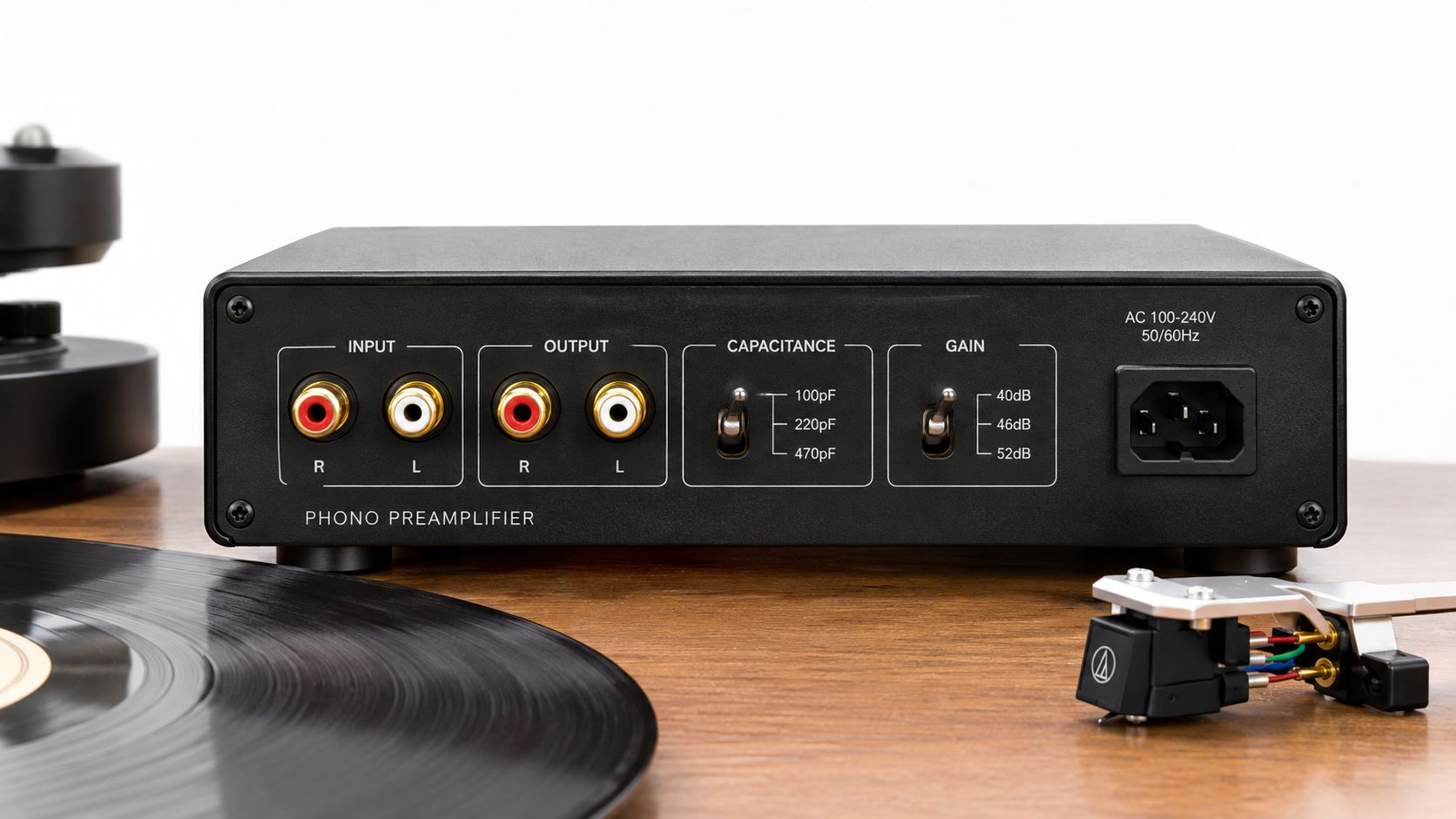 Rear view of a black phono preamplifier on a wooden surface with a vinyl record and cartridge.