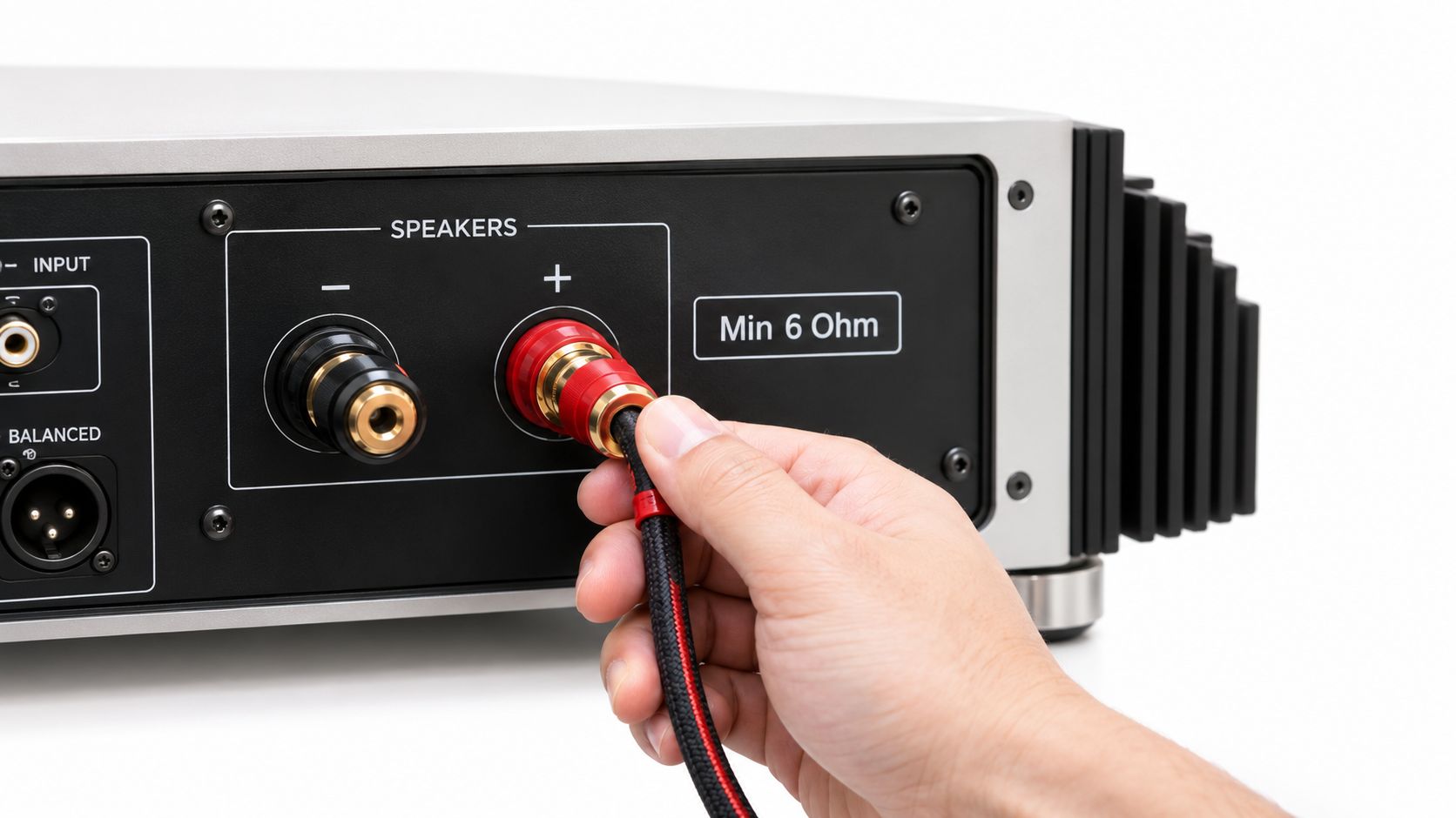 A hand connecting a high-quality audio speaker cable to the positive terminal of an amplifier output.